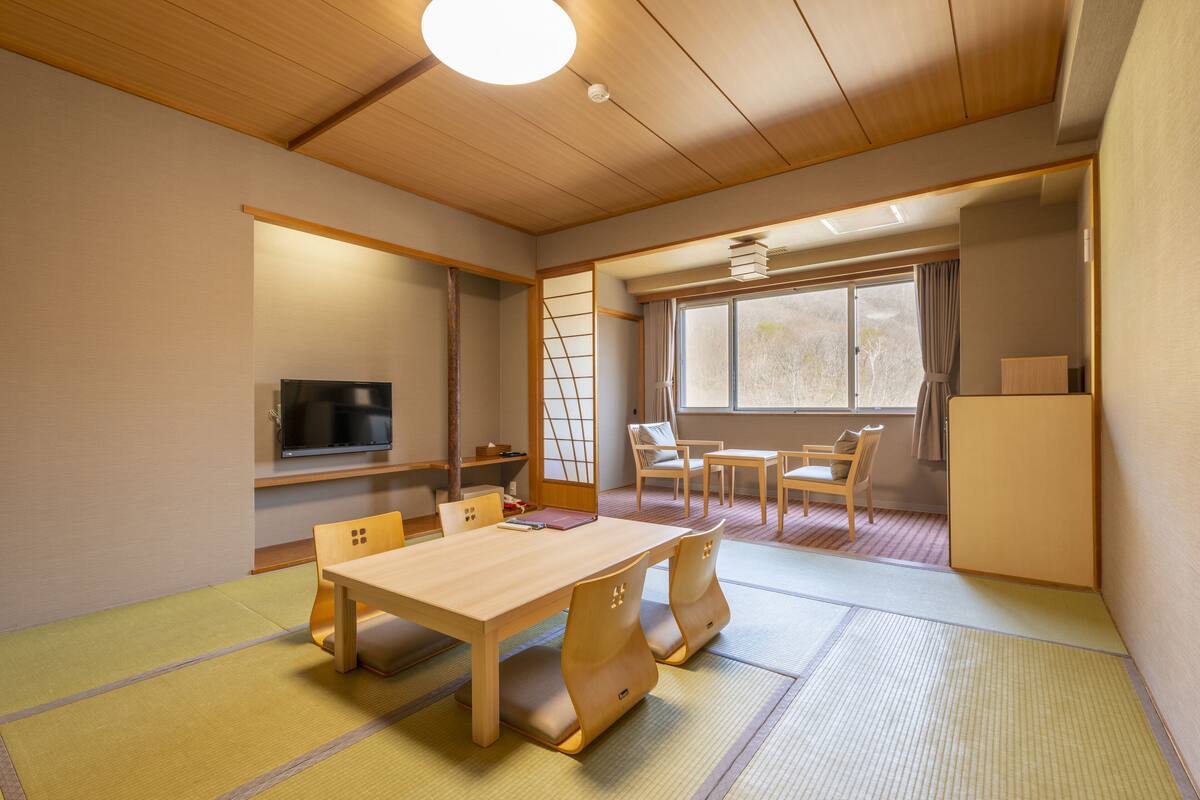 A traditional Japanese-style room with tatami flooring, a low wooden table, and a television on the wall.