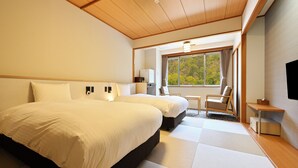 Hotelkamer met twee bedden, een tafeltje, een stoel, een televisie en een raam met uitzicht op bomen.