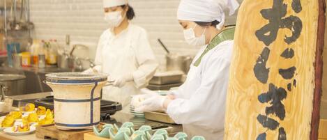 A kitchen with chefs preparing food, a large wooden board with calligraphy, and a tray of food items.