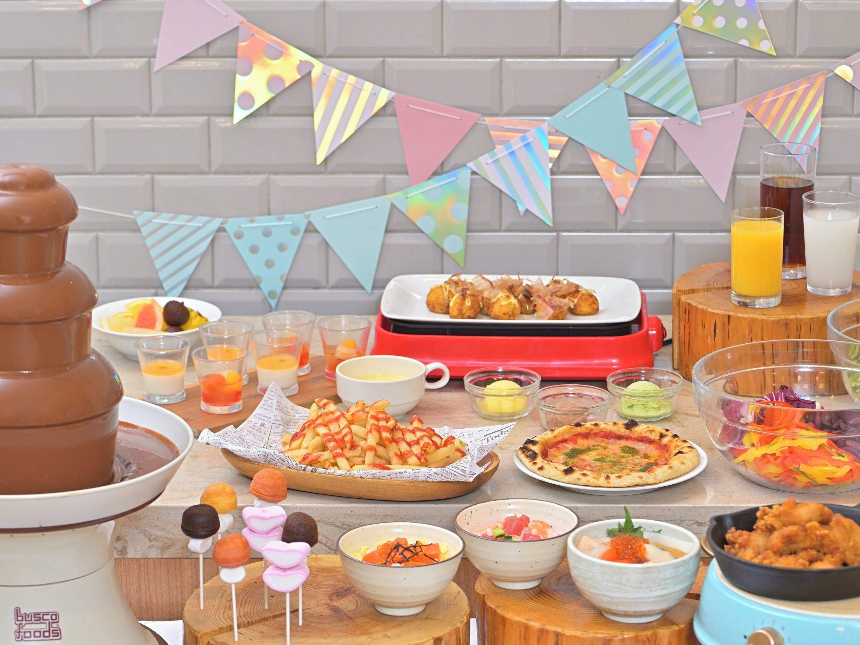 A buffet table with various dishes, including a hot chocolate dispenser, a plate of croissants, and several bowls of food.
