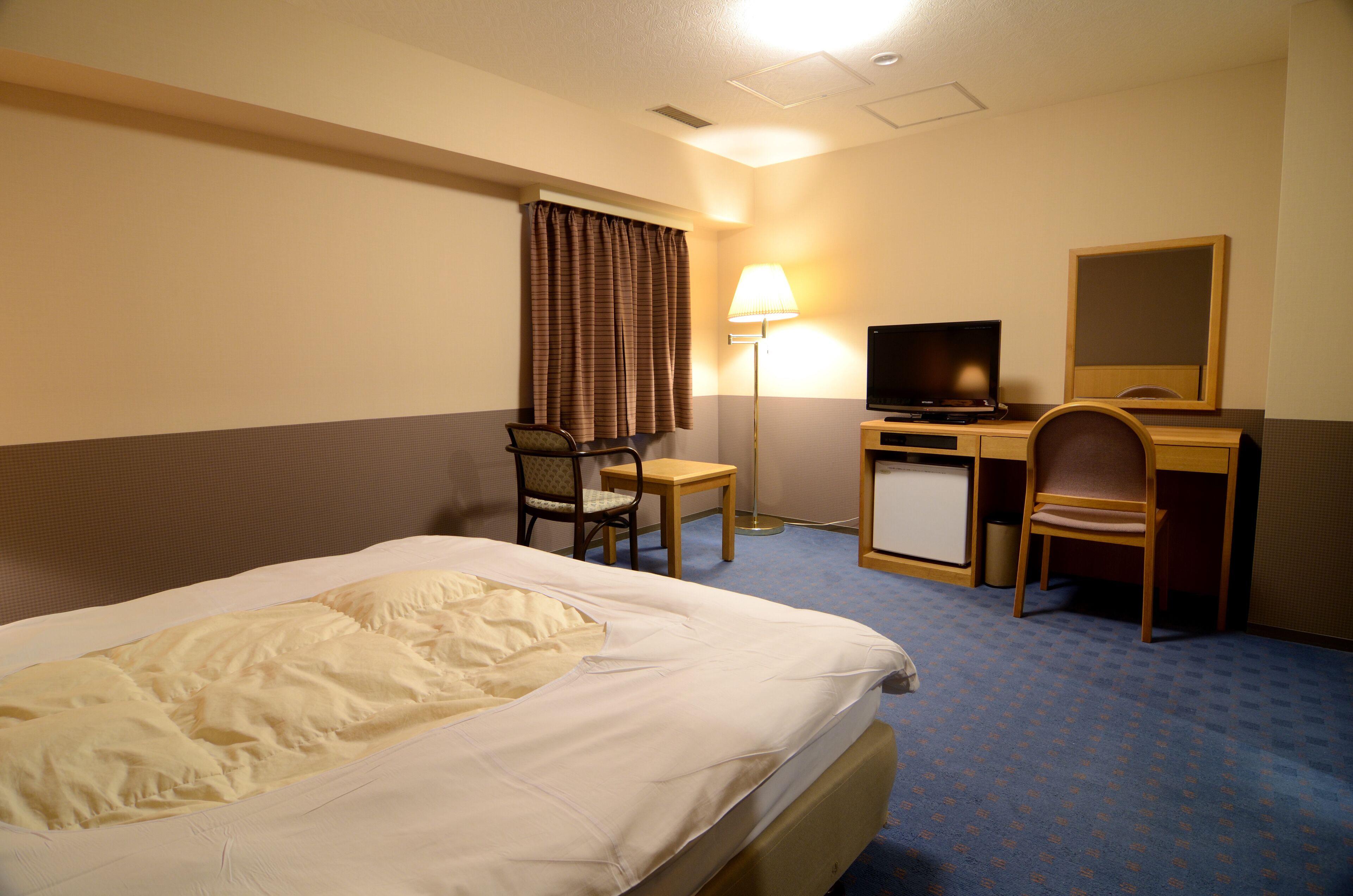 Ein Hotelzimmer mit Bett, Schreibtisch, Stuhl, Fernseher und Lampe.