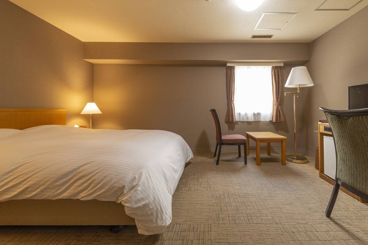 A hotel room with a large bed, a desk, a chair, a lamp, and a television.