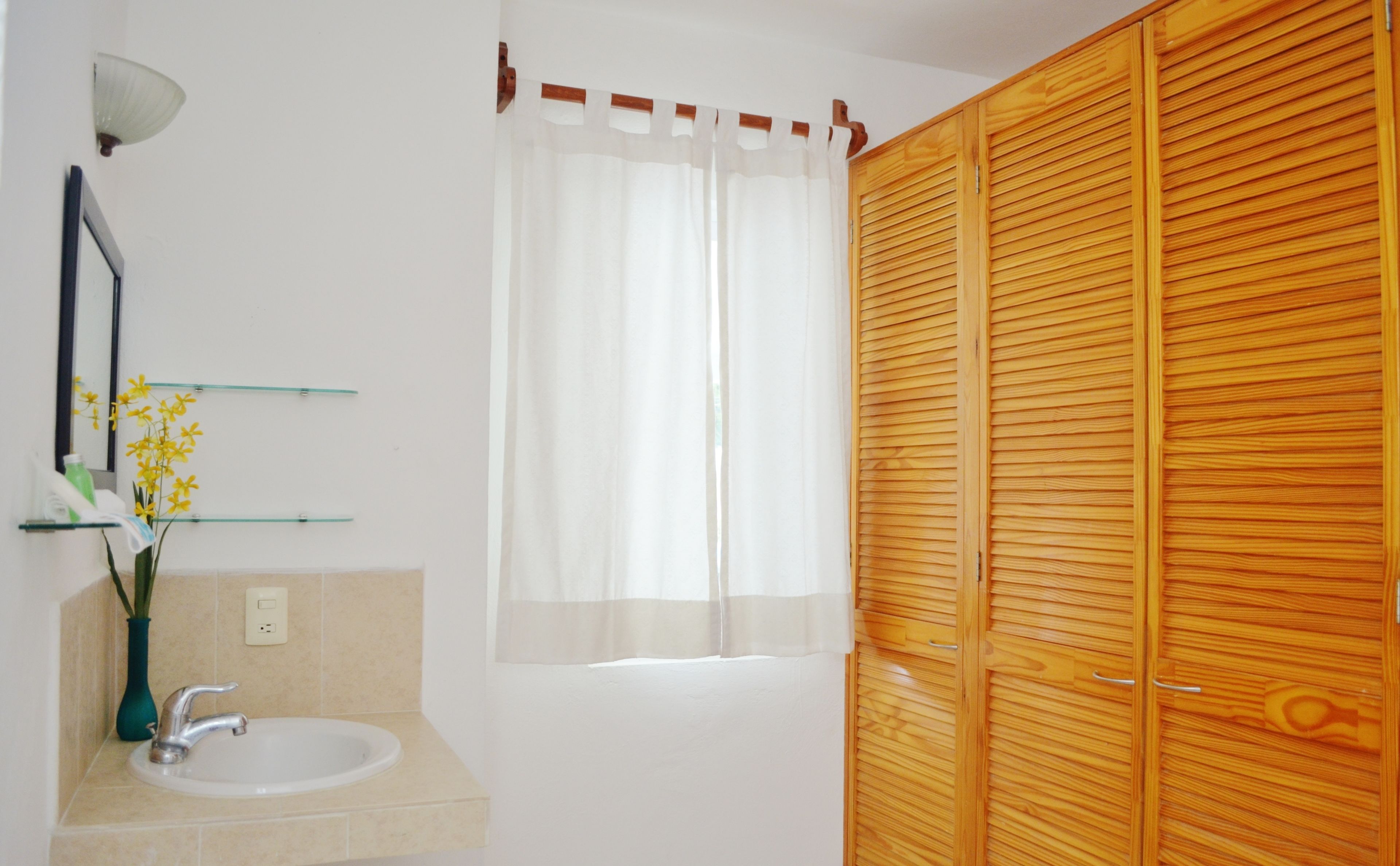 A bathroom with a sink, mirror, and a wooden wardrobe.