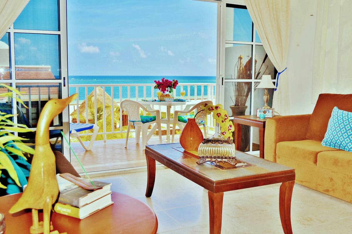 Amplia sala de estar con balcón vistas al mar, que incluye una mesa de centro de madera, un sofá y una mesa de comedor con sillas.