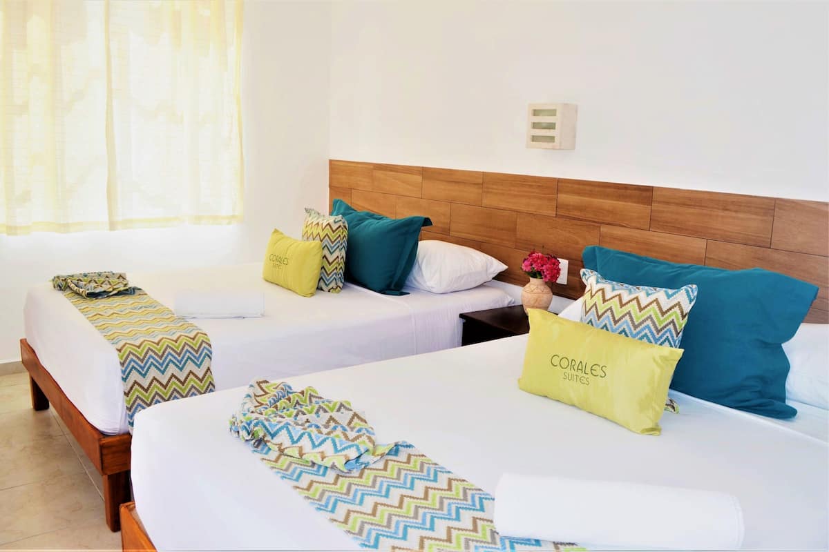 Habitación de hotel con dos camas individuales, cada una con cabecero de madera, ropa de cama blanca y mantas con un colorido estampado en zigzag.