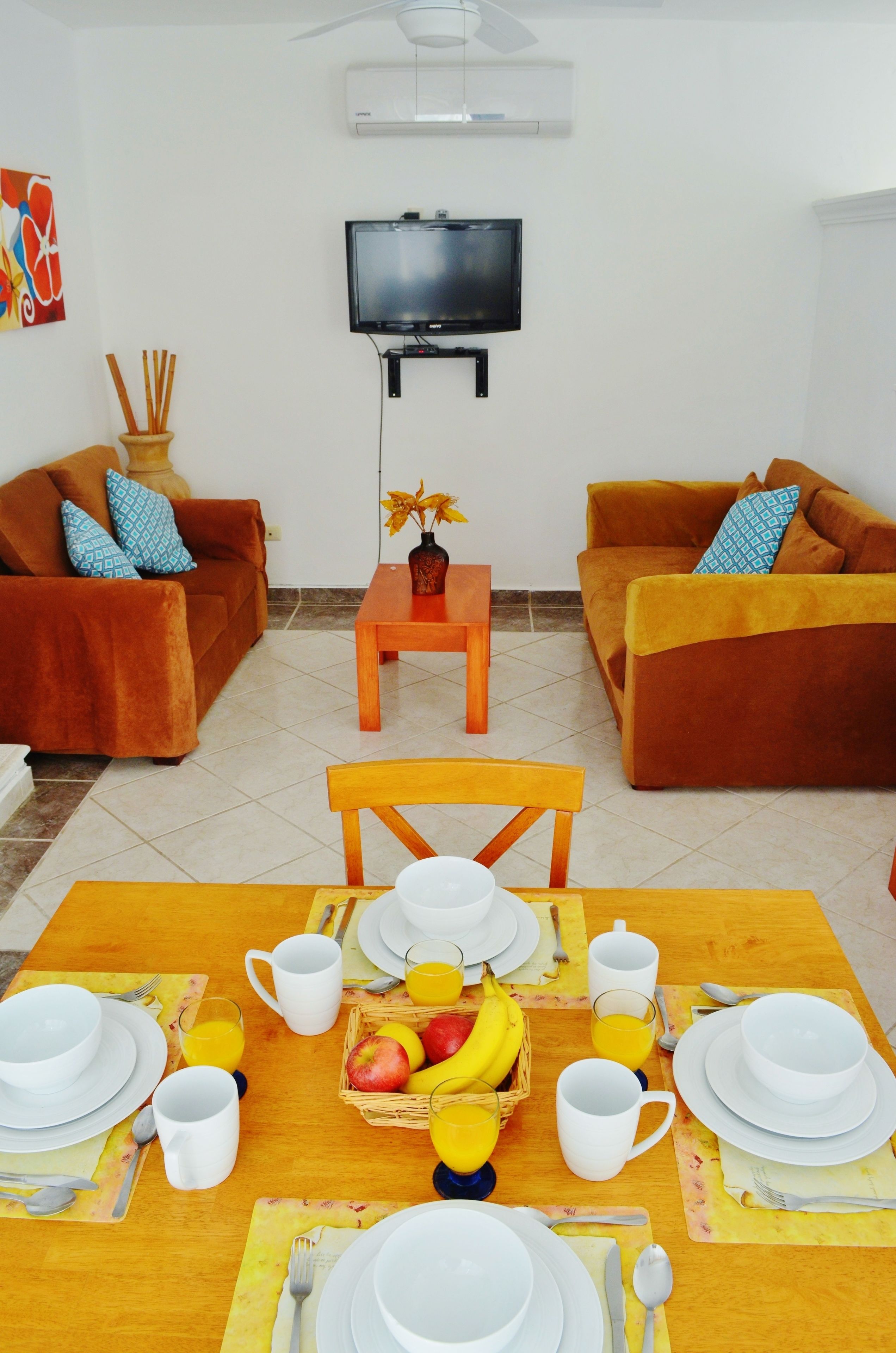 A living room with two sofas, a TV, and a dining table set with plates, cups, and fruit.