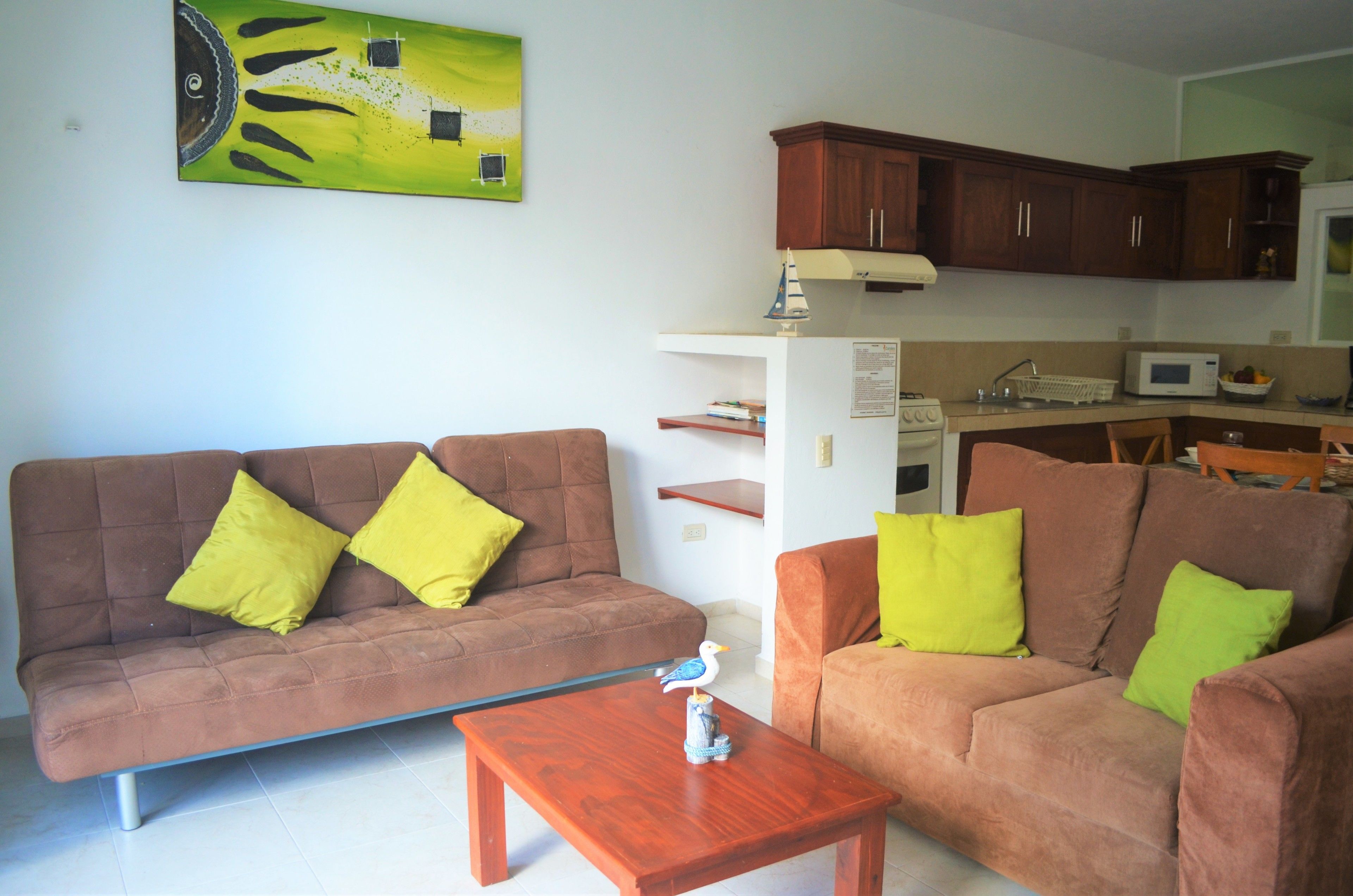 A living room with two brown sofas, each with a green pillow, a wooden coffee table, and a small decorative bird statue.