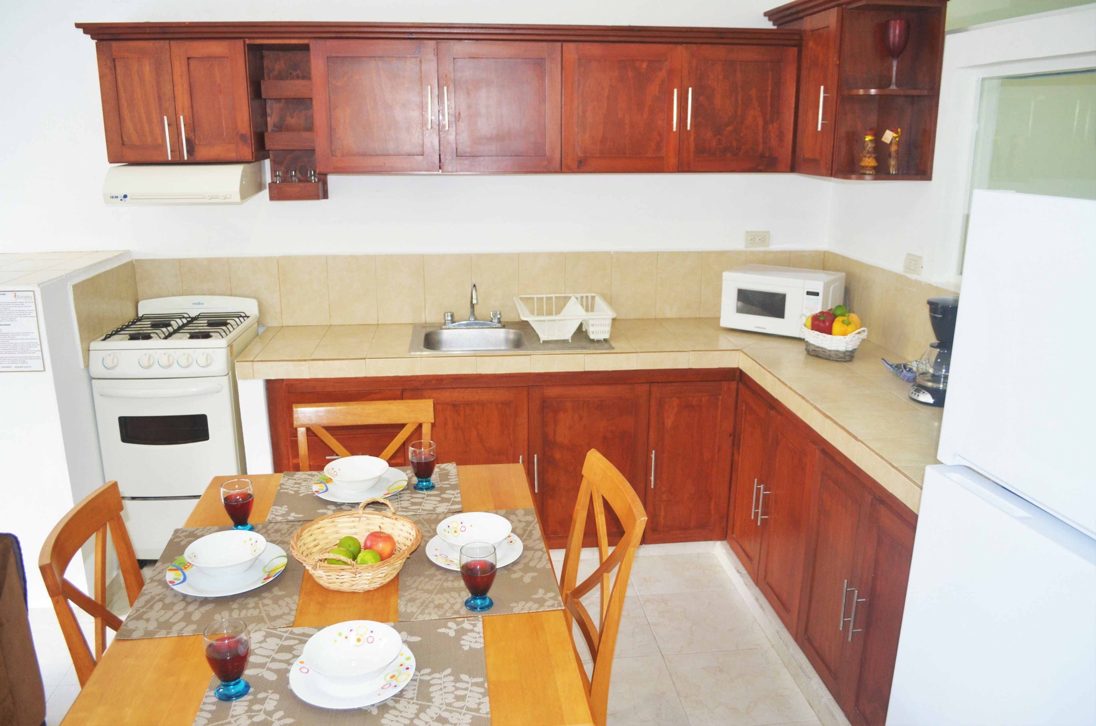 Una cocina con armarios de madera, una estufa, un fregadero y una mesa de comedor dispuesta con platos, vasos y una cesta de fruta.