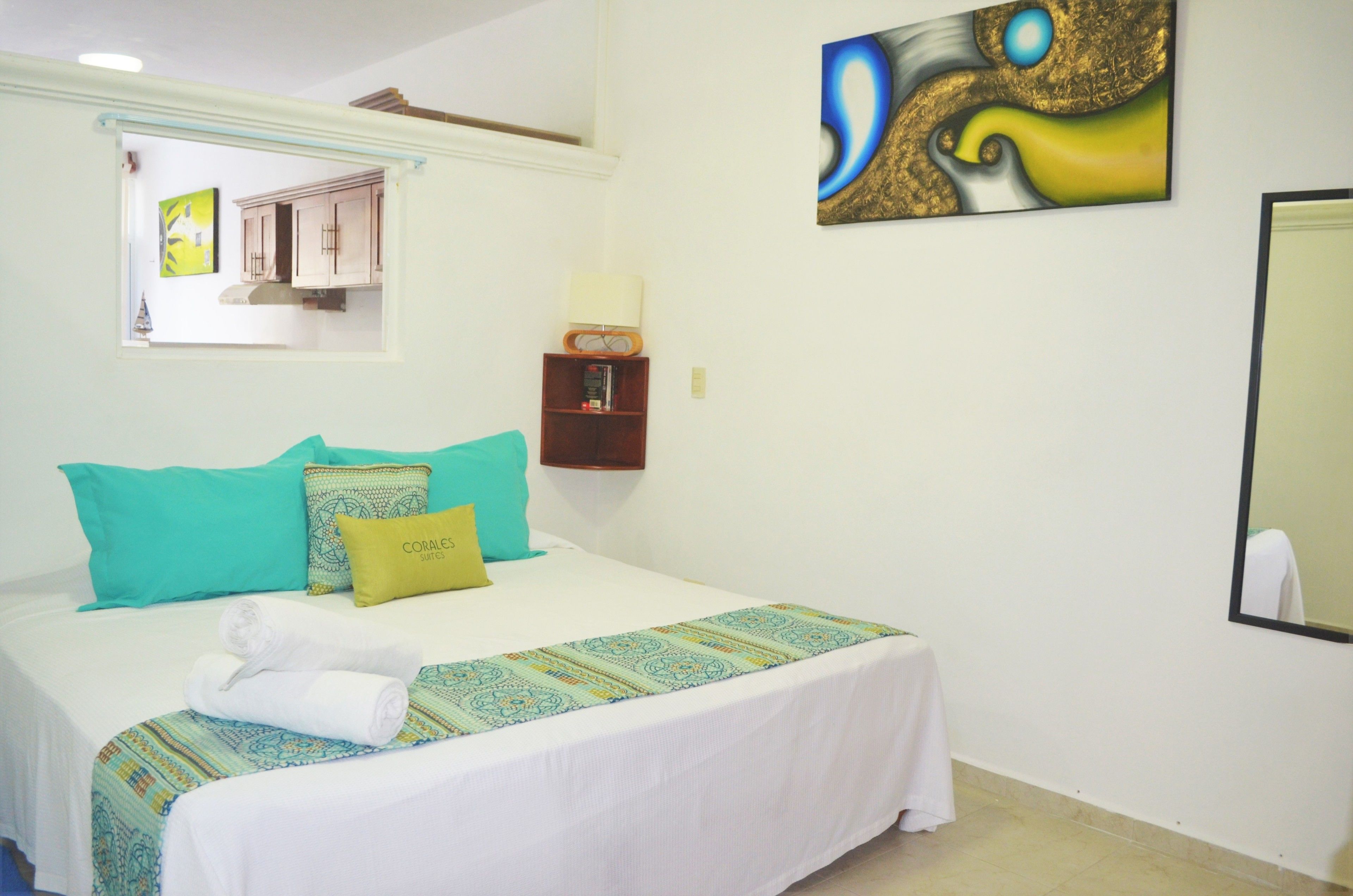 A hotel room with a bed, a nightstand, a wall-mounted lamp, and a painting.