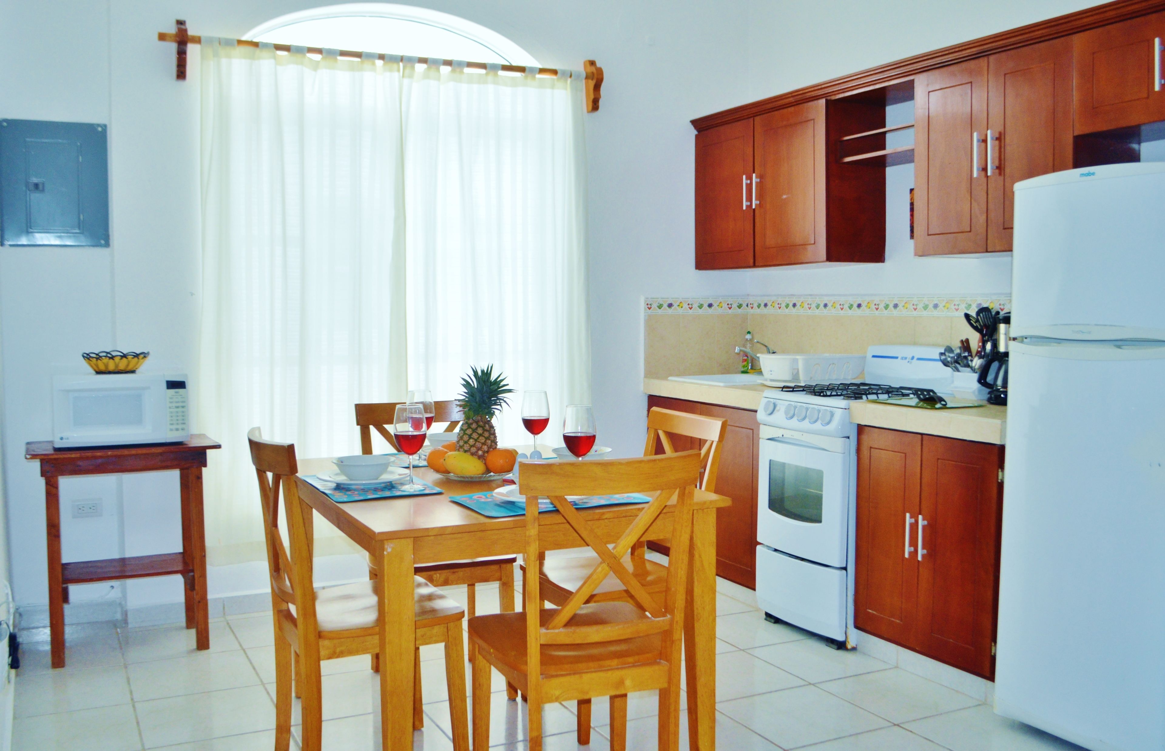 A compact kitchen with wooden cabinets, a white refrigerator, a microwave, and a stove.