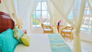 A hotel room with a bed, two chairs, a small table, and a view of the ocean. - Corales Suites (Puerto Morelos)