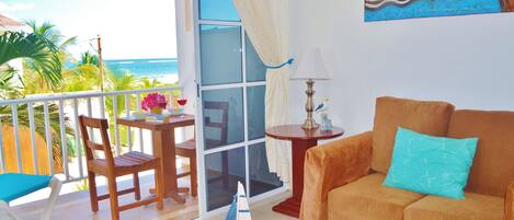 A living room with a sofa, a table with a lamp, a chair, and a view of the ocean.