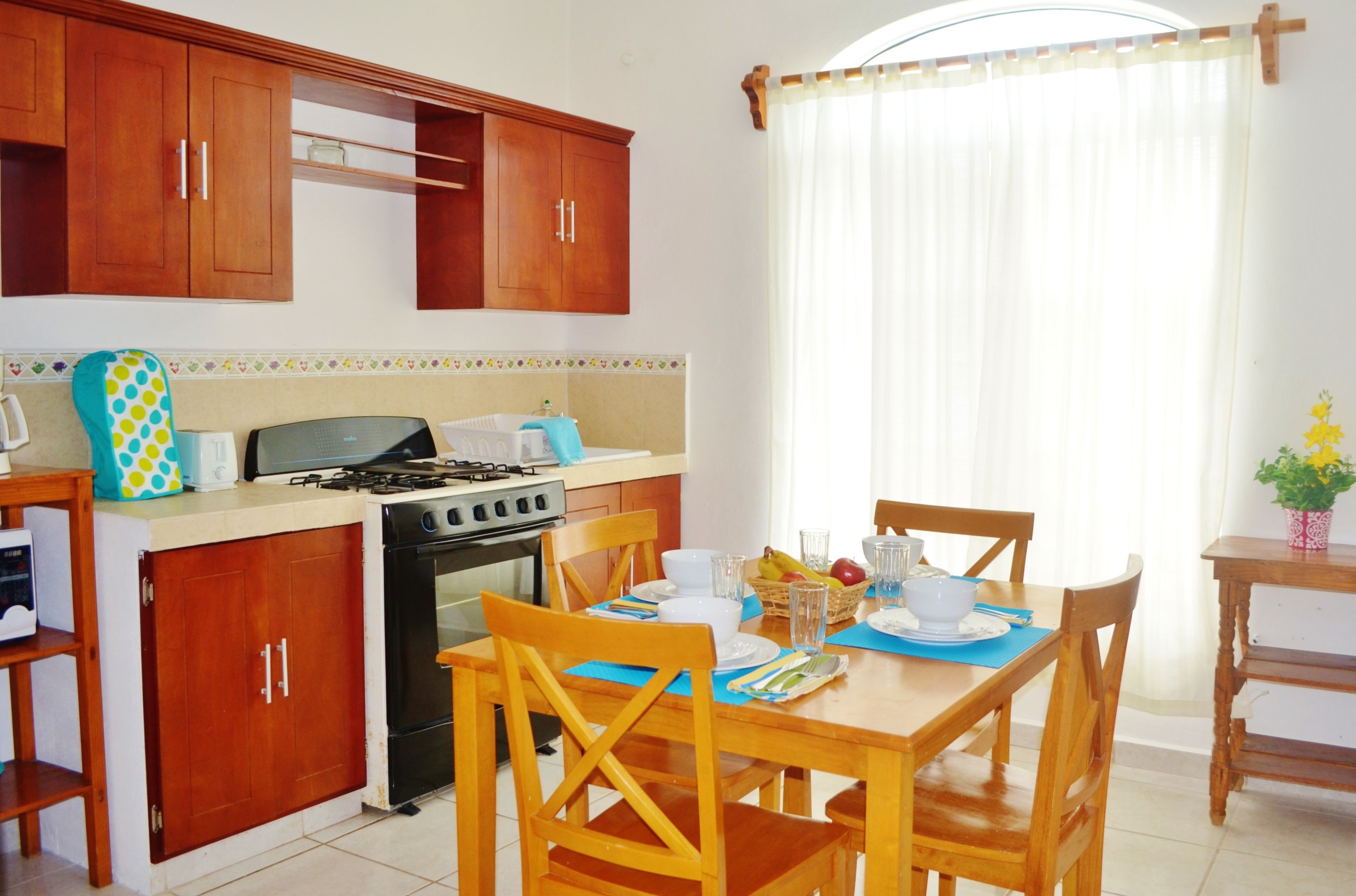 A kitchen with wooden cabinets, a stove, and a dining table set for four.