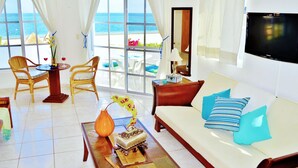 A living room with a sofa, chairs, a coffee table, and a TV. - Corales Suites (Puerto Morelos)
