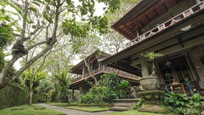 Un edificio tradicional con galería techada, rodeado de exuberante vegetación y un camino de piedra.
