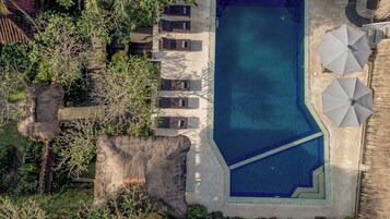 Vista aérea de un complejo turístico con piscina, sillas de descanso y sombrillas.