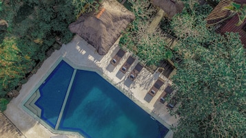 Vista aérea de una piscina con sillas de descanso y una estructura de techo de paja.