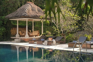 A pool area with lounge chairs, a gazebo, and a thatched roof structure. - Artini 2 Cottages (Ubud)