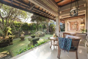 Un jardín tranquilo con un patio que tiene una mesa de madera, sillas y un colgador de luces.