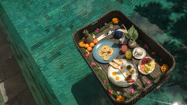 Bandeja de desayuno flotante con diversos alimentos y bebidas sobre una piscina.