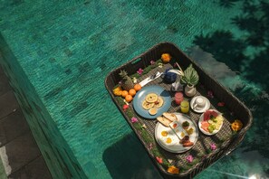 A floating breakfast tray with various food items and drinks over a pool. - Artini Bisma Ubud Hotel (Ubud)