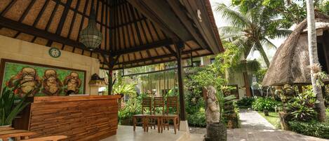 A covered outdoor seating area with wooden benches and a thatched-roof structure.