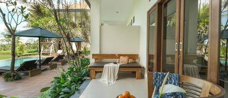 Zona junto a la piscina con sillones de descanso, un banco de madera y una mesa con fruta y una jarrón.