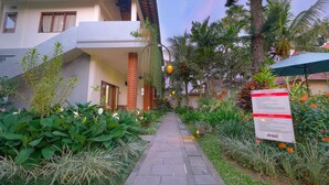 Un sendero conduce a un edificio con balcón, rodeado de vegetación exuberante y palmeras.