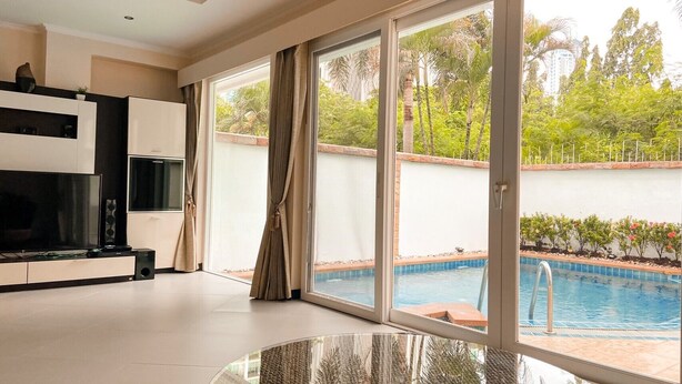 A modern living room with a flat-screen TV, a glass coffee table, and a sliding glass door leading to a pool area. - Hidden Palm Pool Villas (Pattaya)