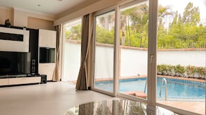 A modern living room with a flat-screen TV, a glass coffee table, and a sliding glass door leading to a pool area. - Hidden Palm Pool Villas (Pattaya)