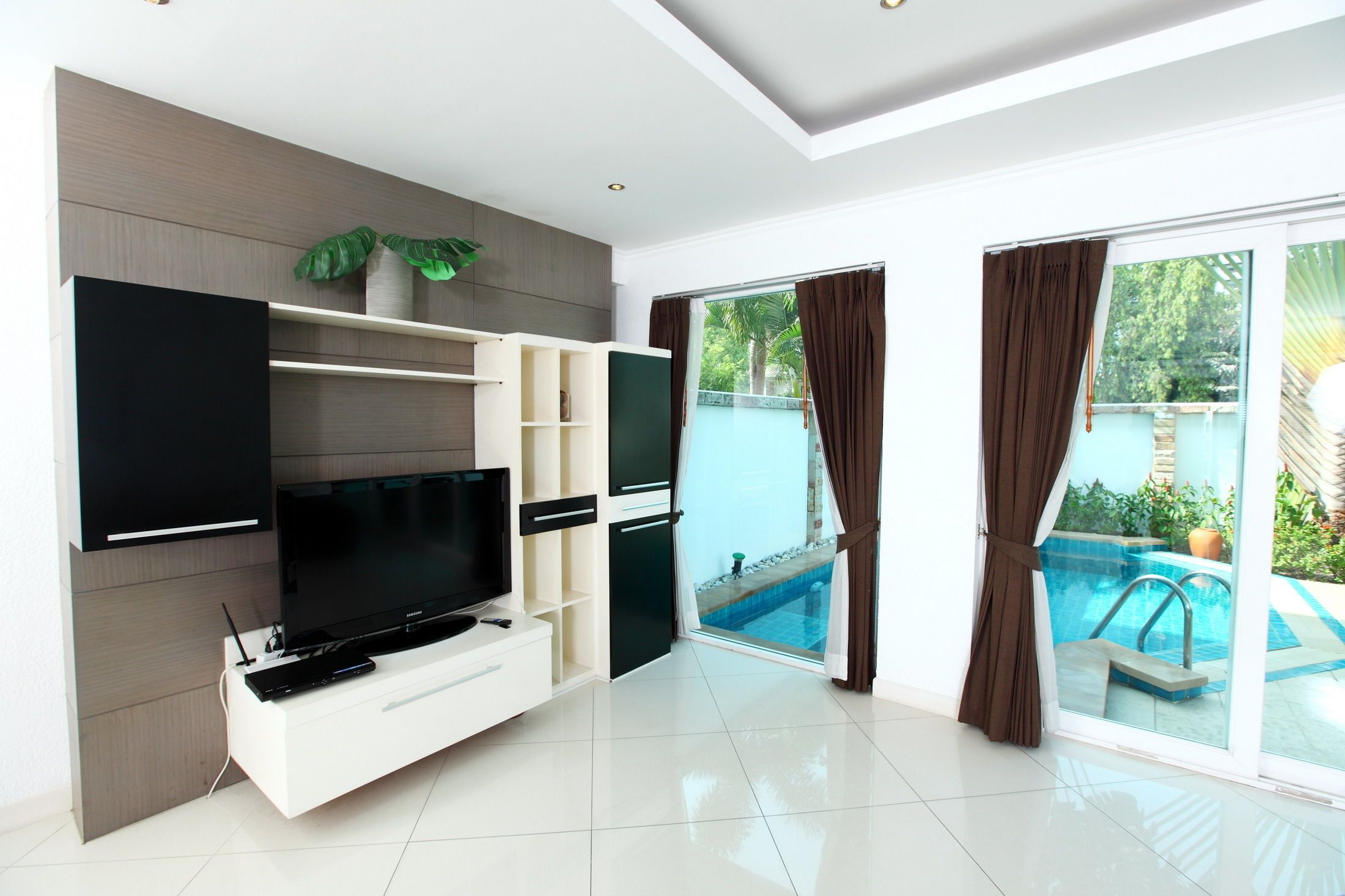 Una sala de estar moderna con un televisor de pantalla plana, estanterías empotradas y un ventanal corredizo que da a una piscina.