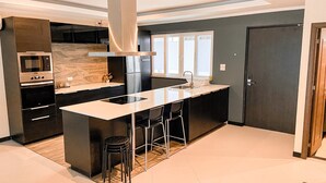 A modern kitchen with a central island, stainless steel appliances, and a large window providing natural light. - Hidden Palm Pool Villas (Pattaya)