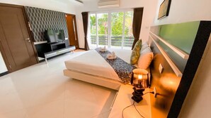 A modern bedroom with a bed, a TV, and a balcony with a view of greenery. - Hidden Palm Pool Villas (Pattaya)