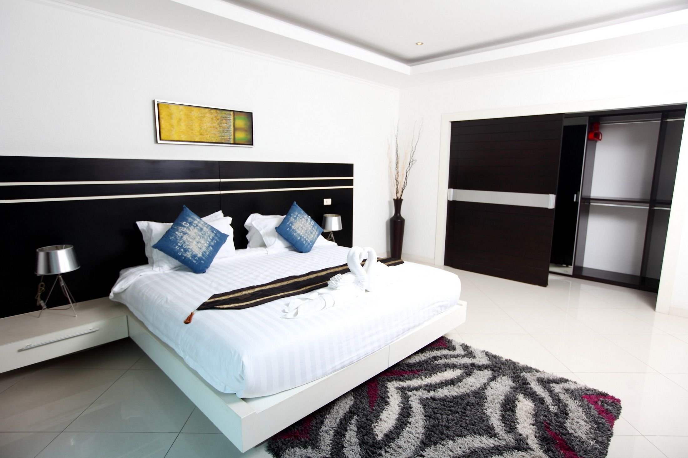 Un dormitorio moderno con una cama grande, una mesita de noche, una lámpara y un jarrón decorativo.