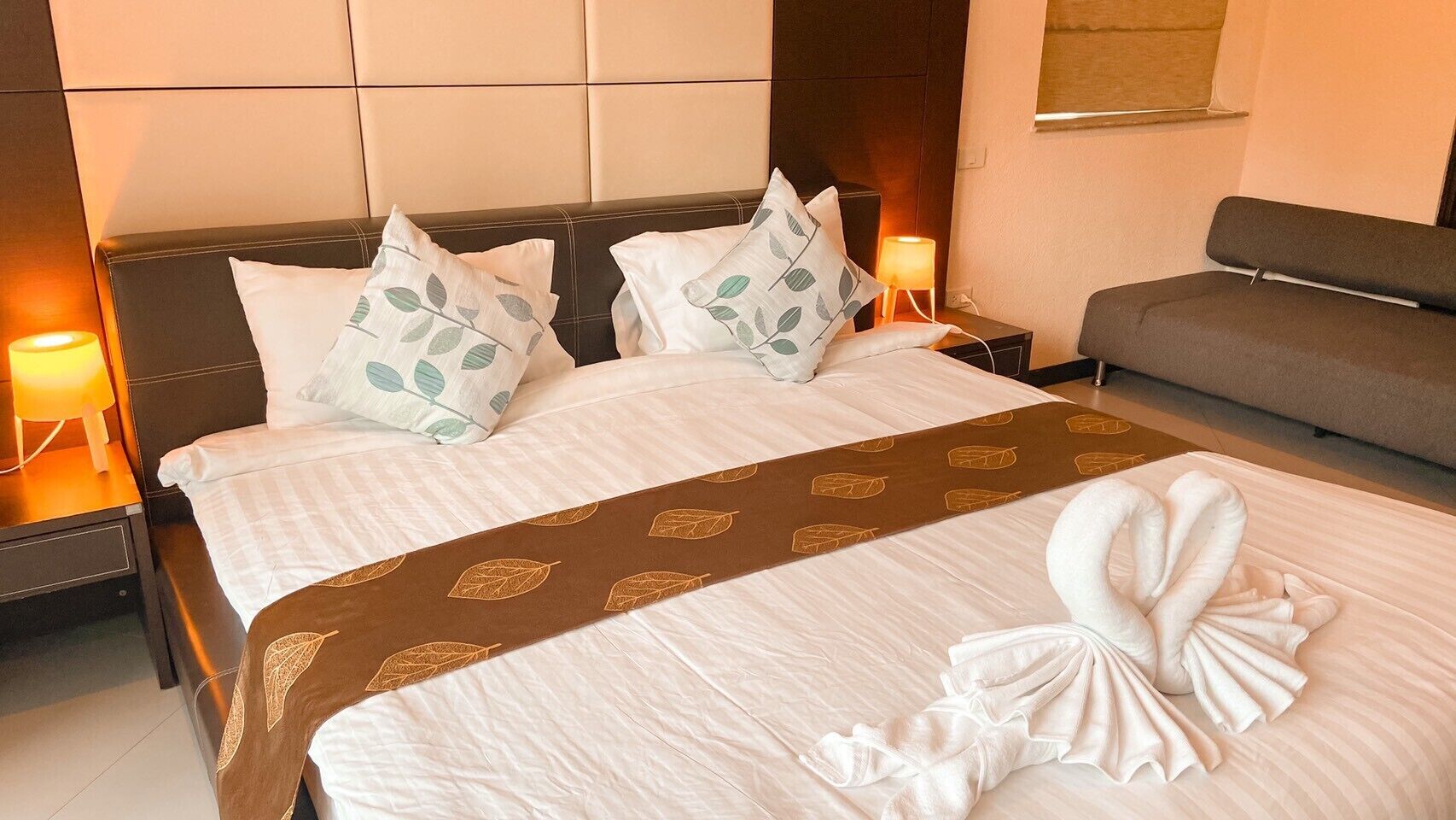 A hotel room with a large bed, two bedside tables with lamps, a sofa, and a decorative towel arrangement on the bed.