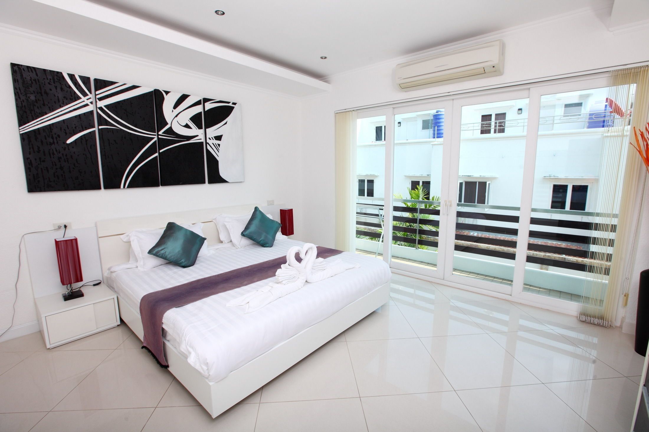 A modern hotel room with a large bed, a view of the outside balcony, and a contemporary abstract painting on the wall.