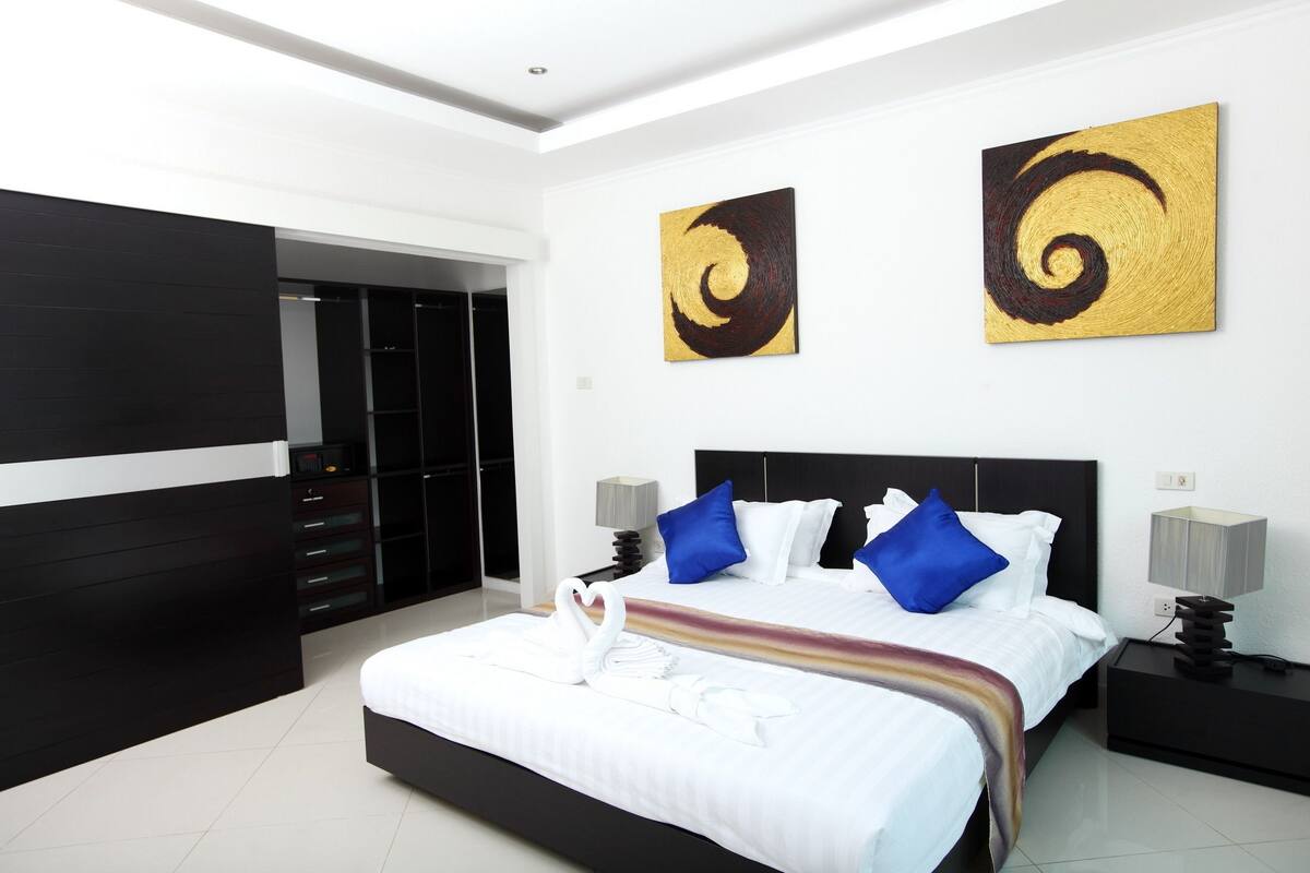 A modern hotel room with a large bed, black and white decor, two wall art pieces, and a view of a wardrobe.