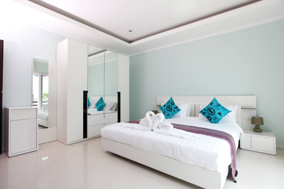 A modern bedroom with a large bed, a wardrobe, and a mirror.