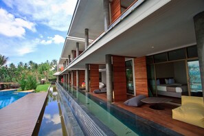Un hotel moderno con una piscina larga, terraza de madera y zonas de estar al aire libre.