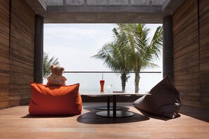 Una habitación moderna con un ventanal grande, una mesa con una bebida y dos pufs.