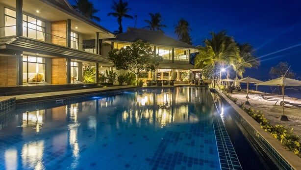 A modern hotel with a swimming pool, large windows, and palm trees. - Na Tara Resort (Ko Chang)
