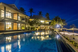 Un hotel moderno con piscina, ventanas amplias y palmeras.