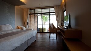 A hotel room with a large bed, a desk with a TV, a chair, and a view of palm trees through the window. - Na Tara Resort (Ko Chang)