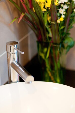 A bathroom sink with a chrome faucet and a vase of flowers in the background. - Ploen Pattaya Residence by Tolani (Pattaya)