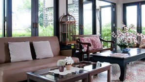 A living room with a brown sofa, a wooden chair, a coffee table, and a bookshelf. - Ploen Pattaya Residence by Tolani (Pattaya)