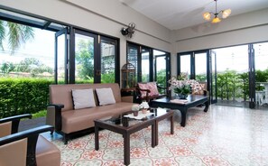A spacious room with a sofa, chairs, a coffee table, and a view of greenery outside. - Ploen Pattaya Residence by Tolani (Pattaya)