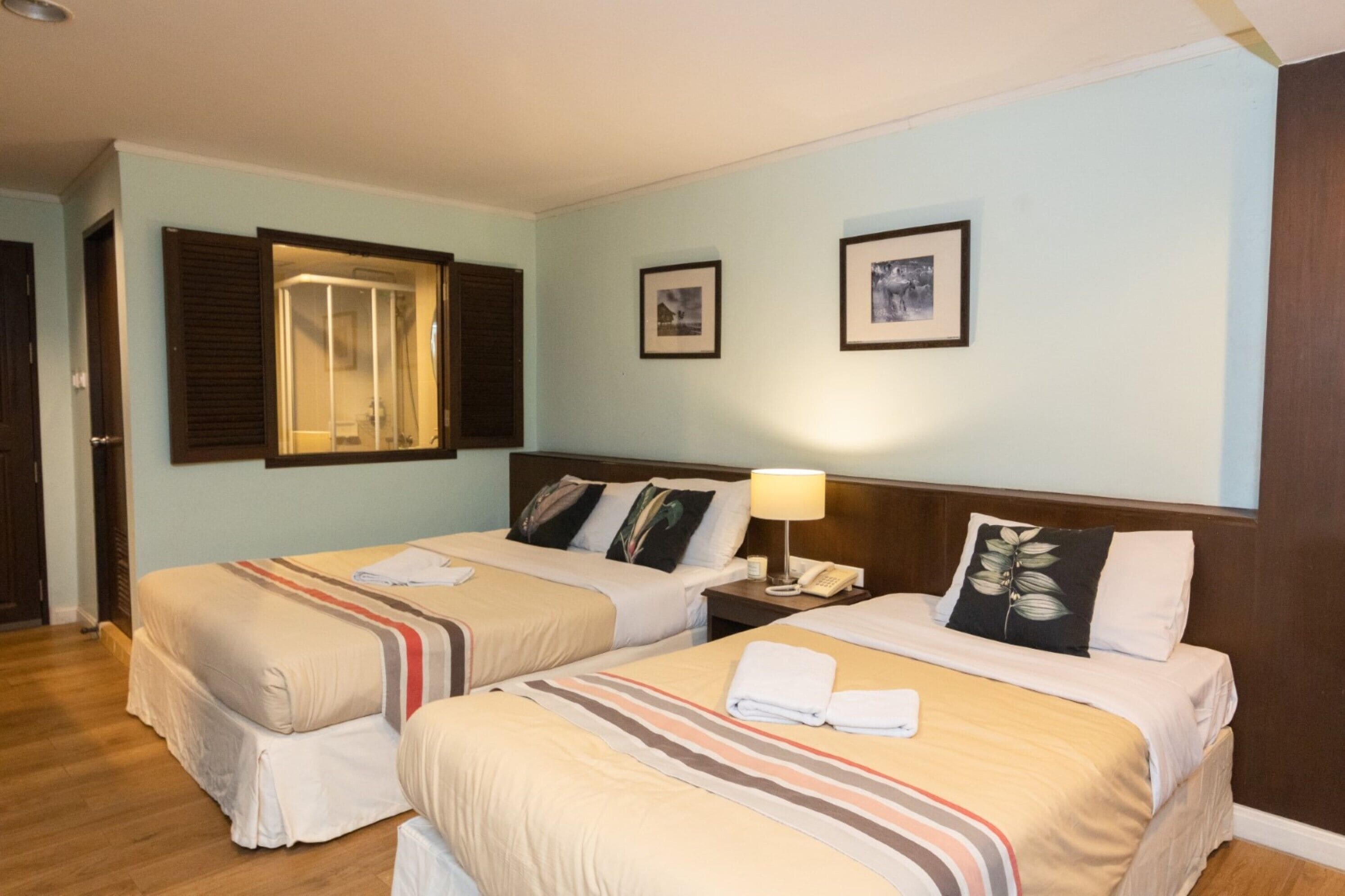 Ein Hotelzimmer mit zwei Betten, Holzboden und einem durchgehenden Türrahmen sichtbaren Badezimmer.