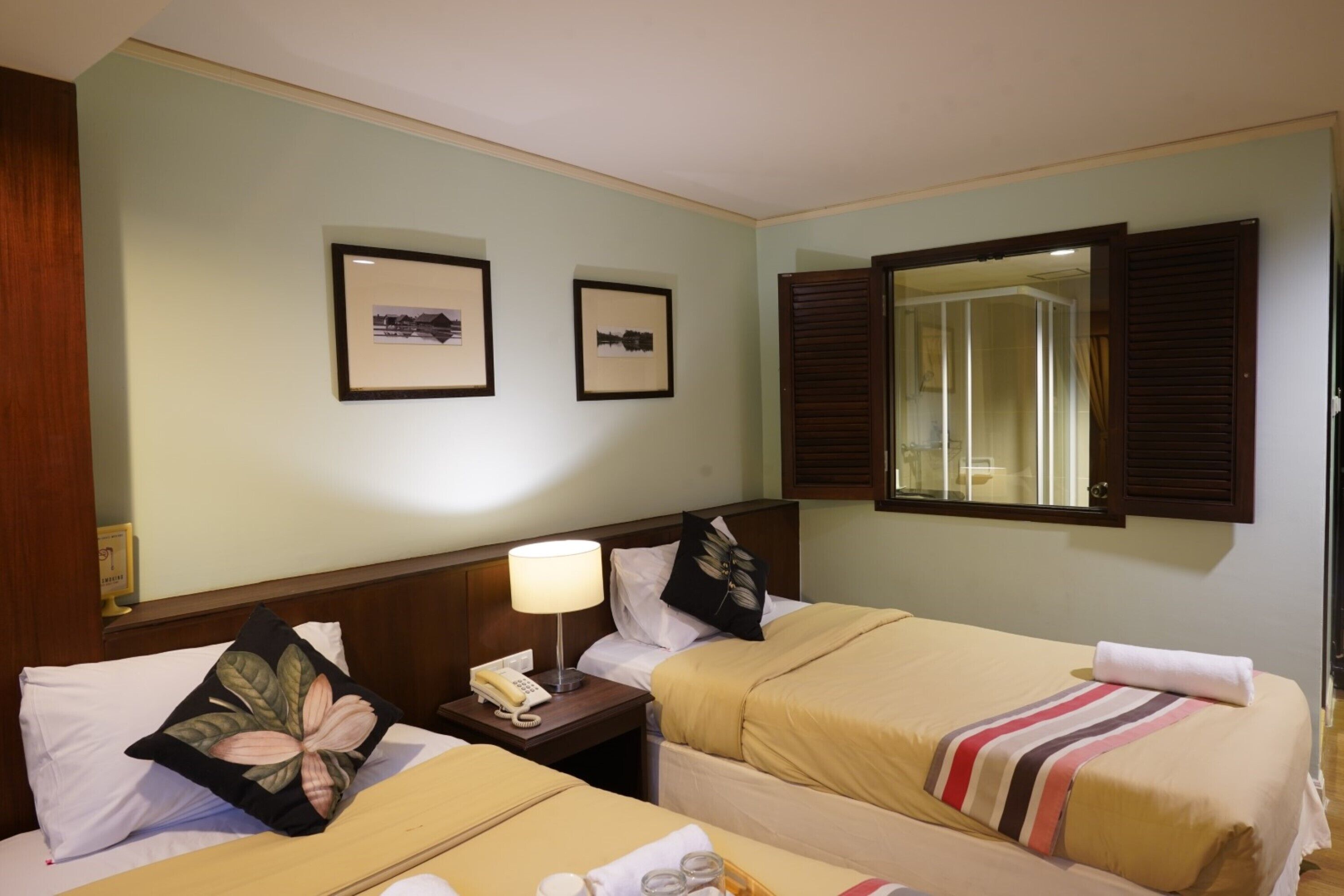 Una camera d'albergo con due letti, un comodino con una lampada e quadri appesi al muro.