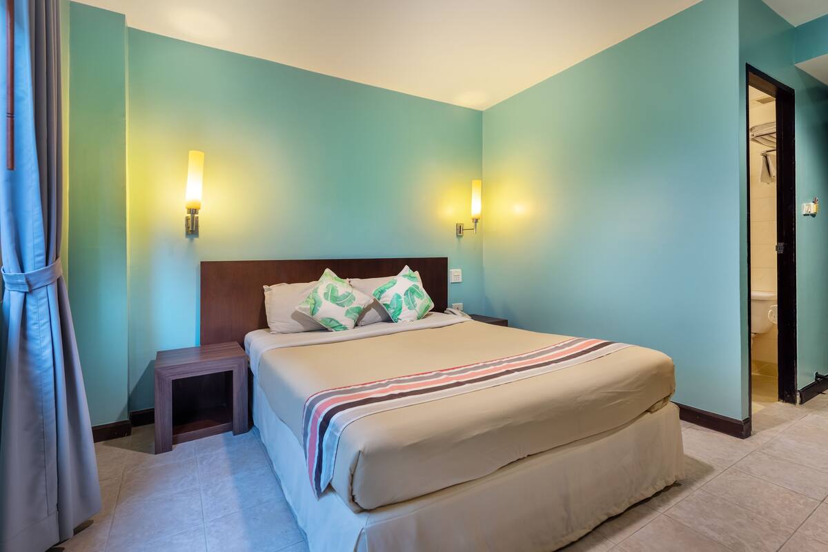 A neatly made bed with a striped blanket, two bedside lamps, and a headboard with decorative pillows.