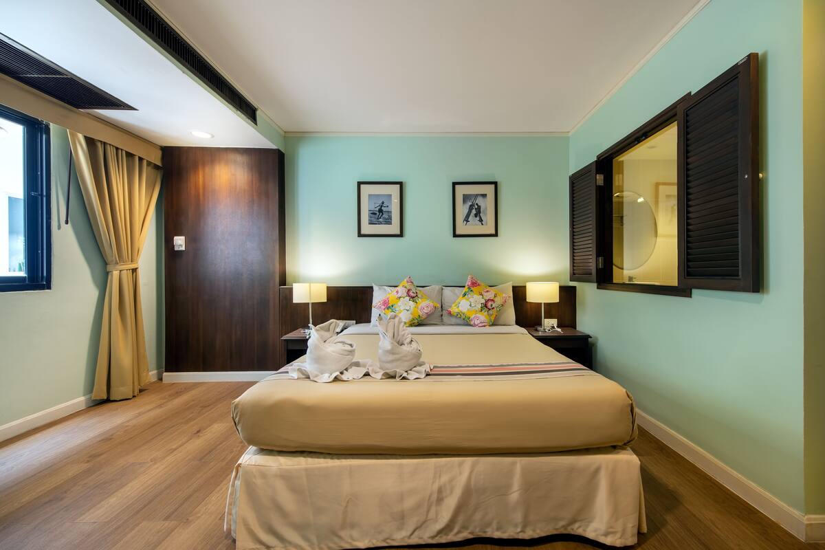 A hotel room with a large bed, two bedside tables with lamps, a wardrobe, and a large mirror.